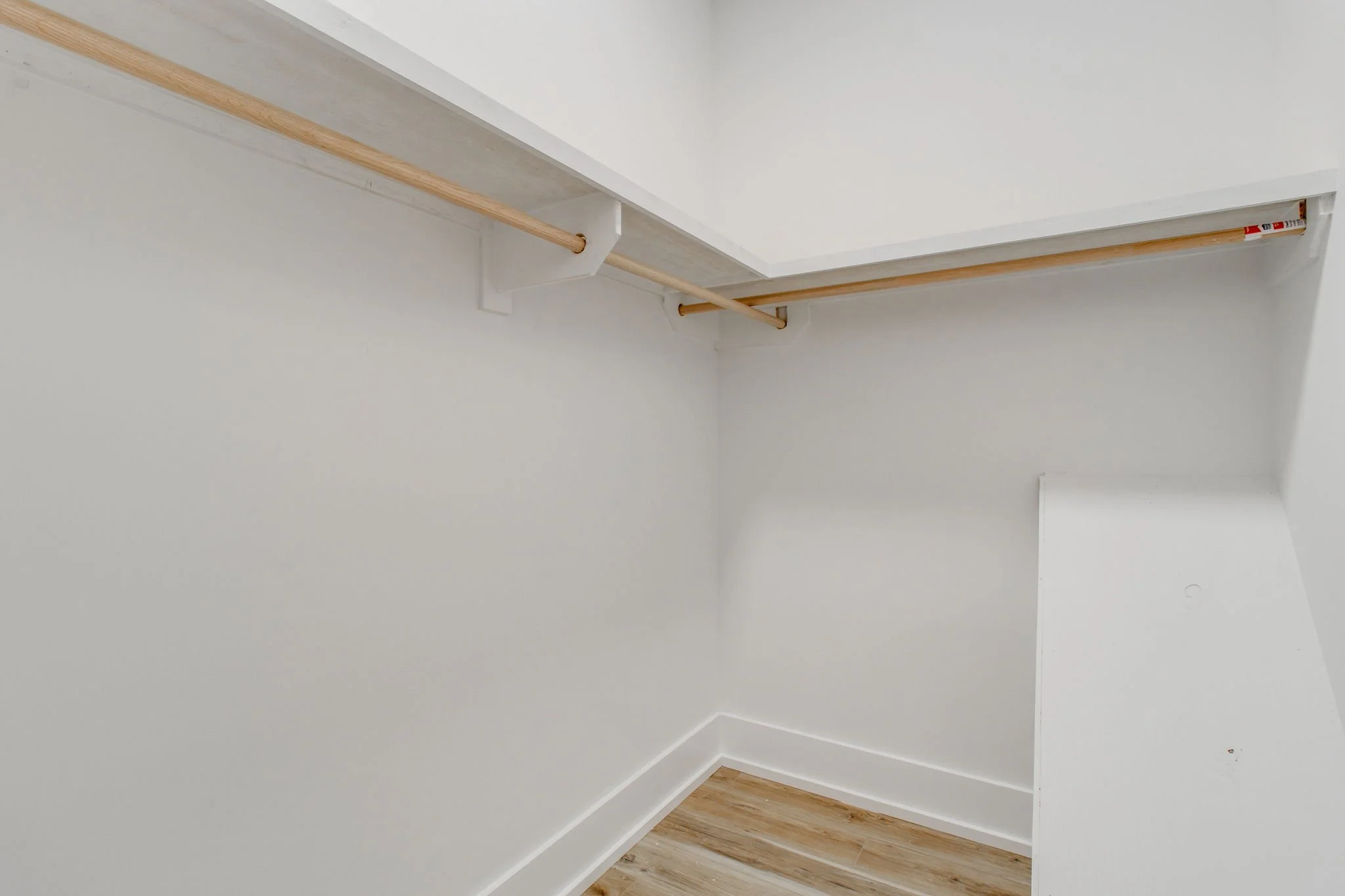 empty white walk-in closet with wooden rods and light wood flooring