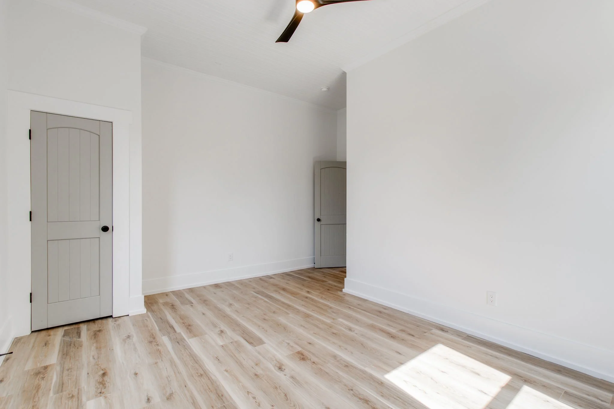Empty room with light wood flooring, white walls, and a ceiling fan.