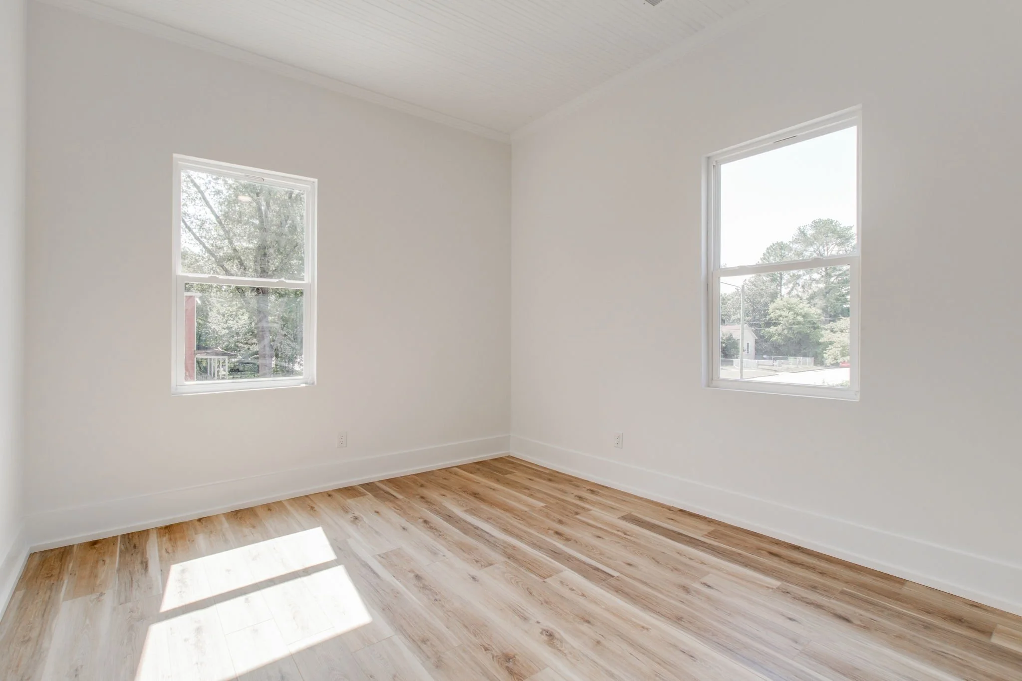 Empty room with white walls and wooden floor, featuring two windows.