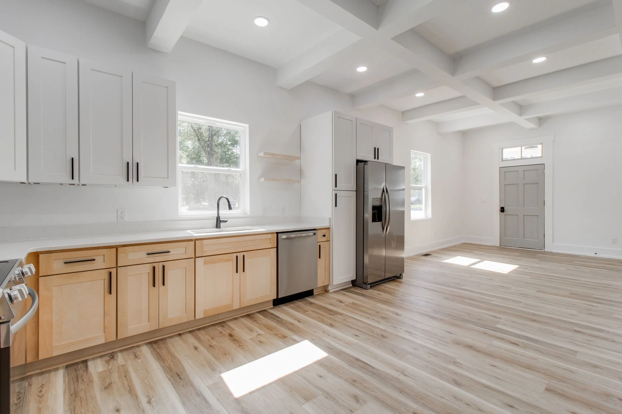 Modern kitchen with wooden cabinets, stainless steel refrigerator, light wood flooring, white walls, and ceiling with recessed lighting.