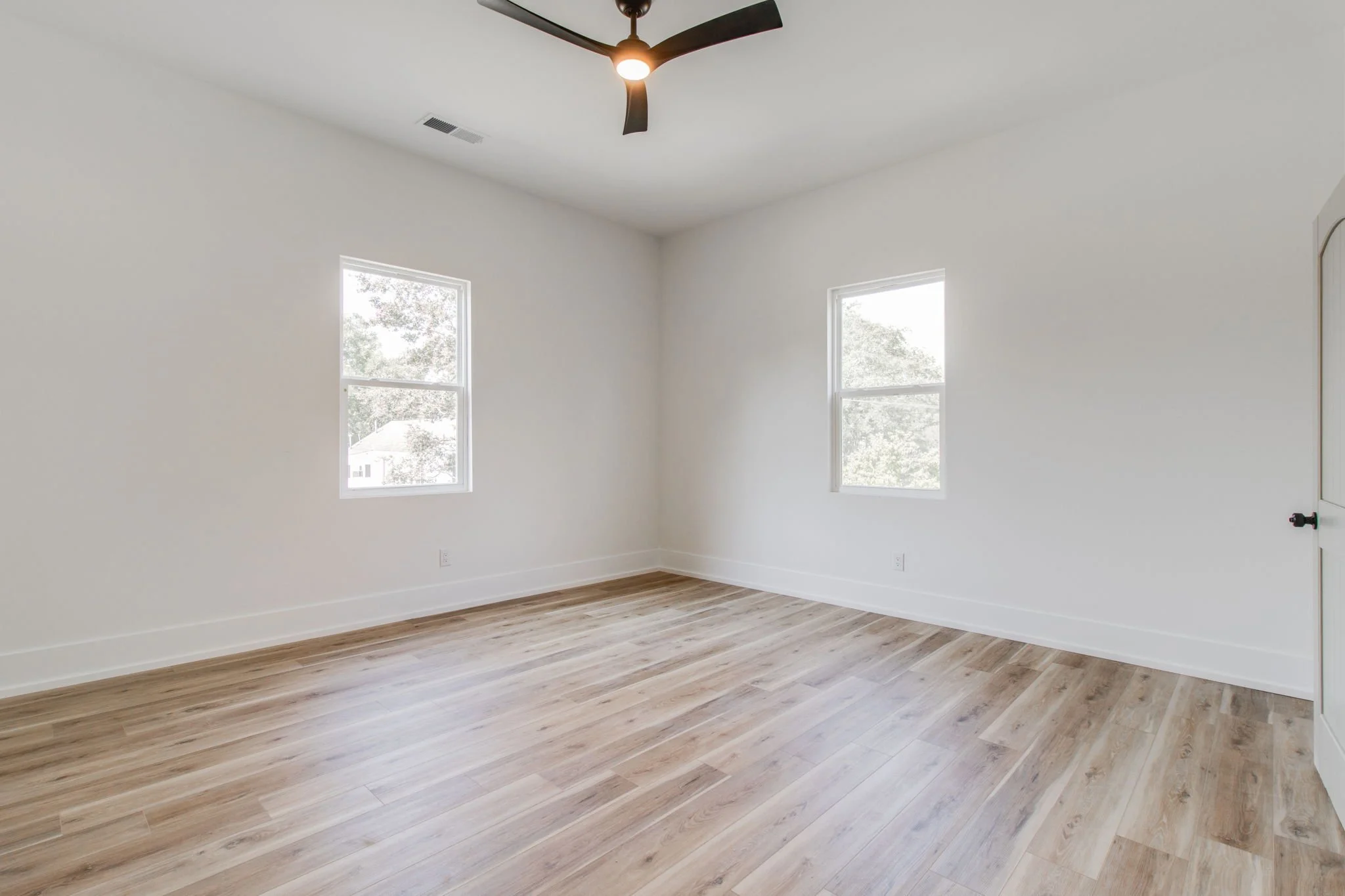 Empty room with wood flooring, two windows, white walls, and a ceiling fan.