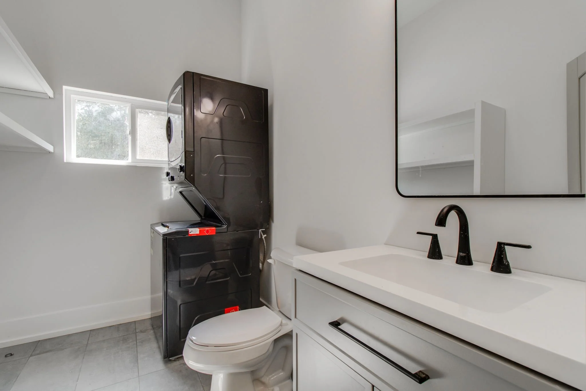 Modern bathroom with toilet, sink, and stacked washer-dryer unit.