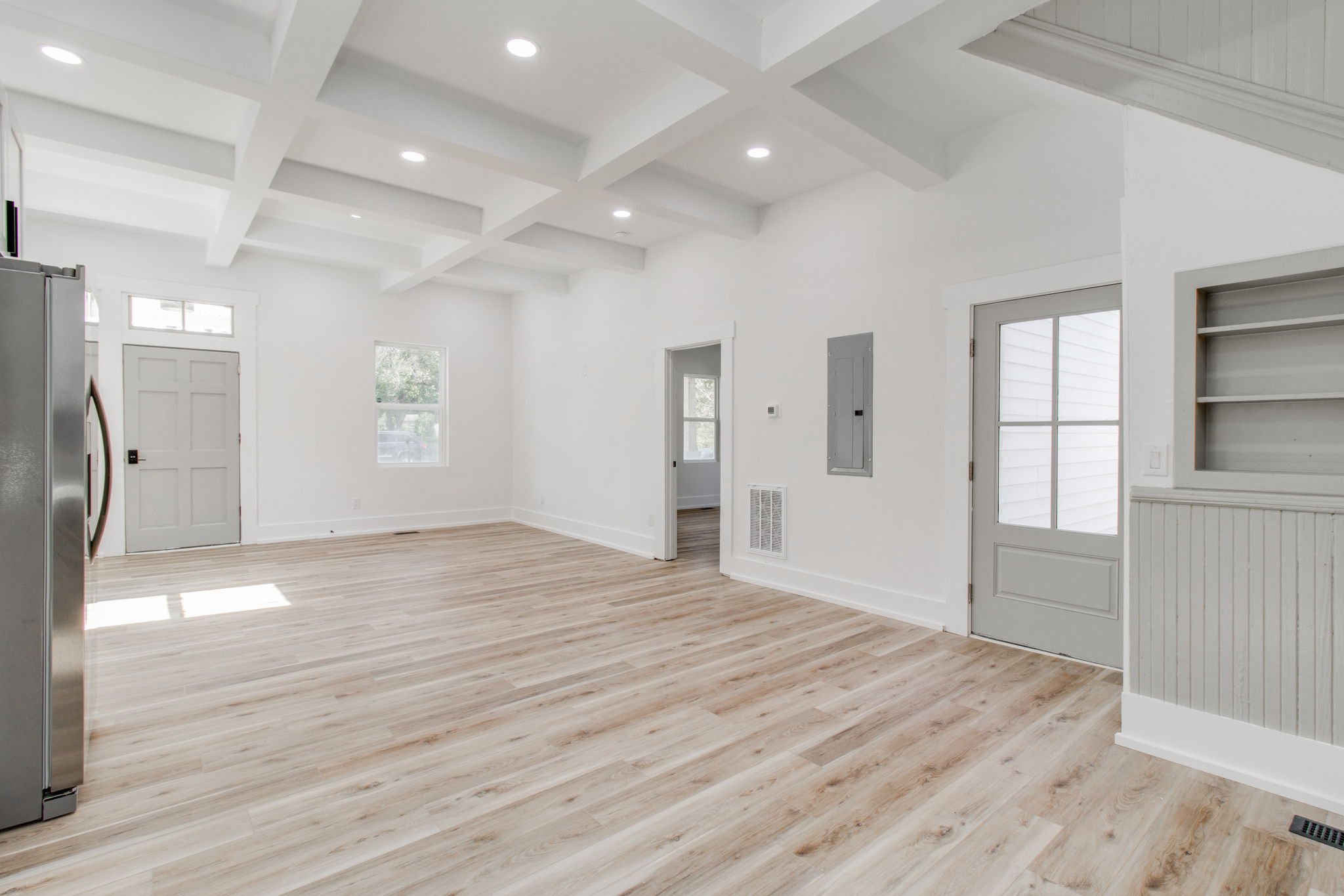 Modern empty room with wooden flooring, gray door, and white walls and ceiling with beams.