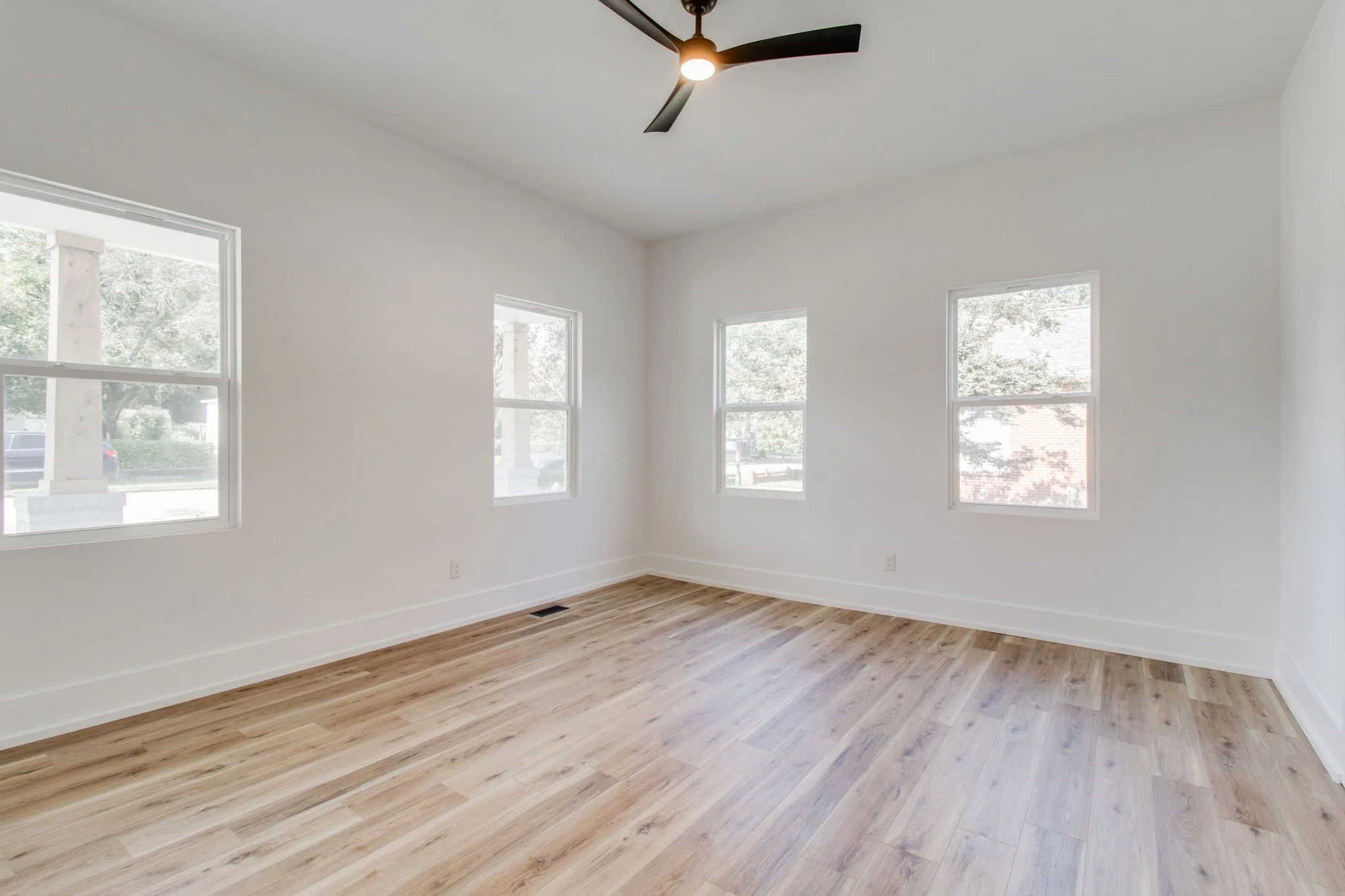 Empty room with three windows, wooden floor, and ceiling fan.