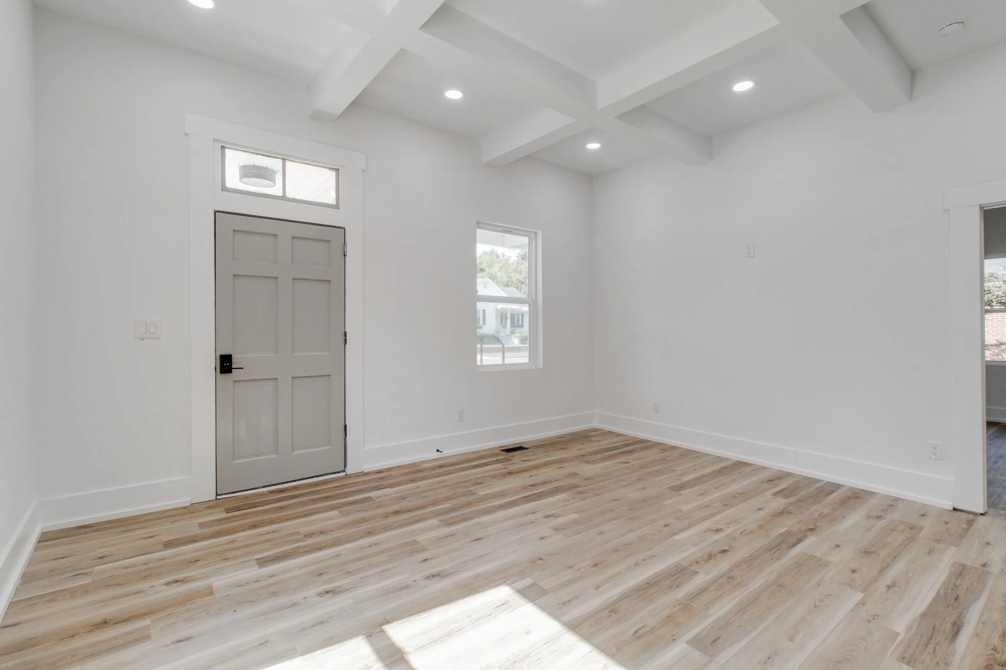 Empty room with hardwood floors, white walls, gray door, and coffered ceiling design.