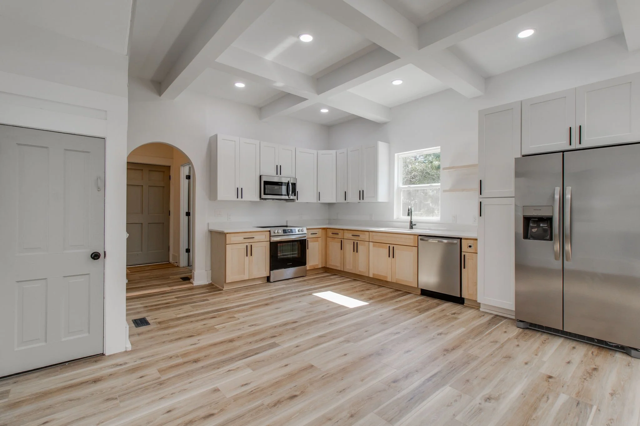 Modern kitchen with white cabinets, stainless steel appliances, light wood flooring, and recessed lighting.
