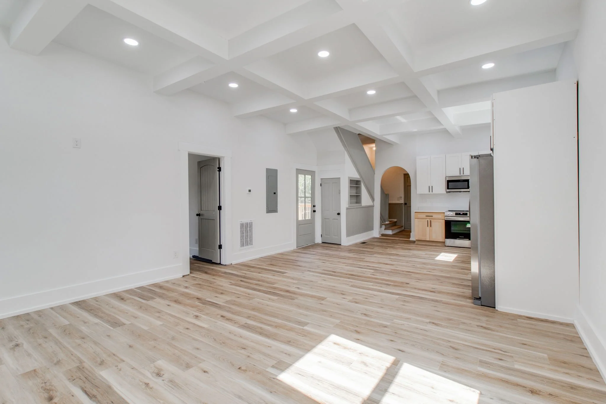 Modern open-plan living room and kitchen with light wood flooring, white walls, recessed lighting, and contemporary cabinetry.