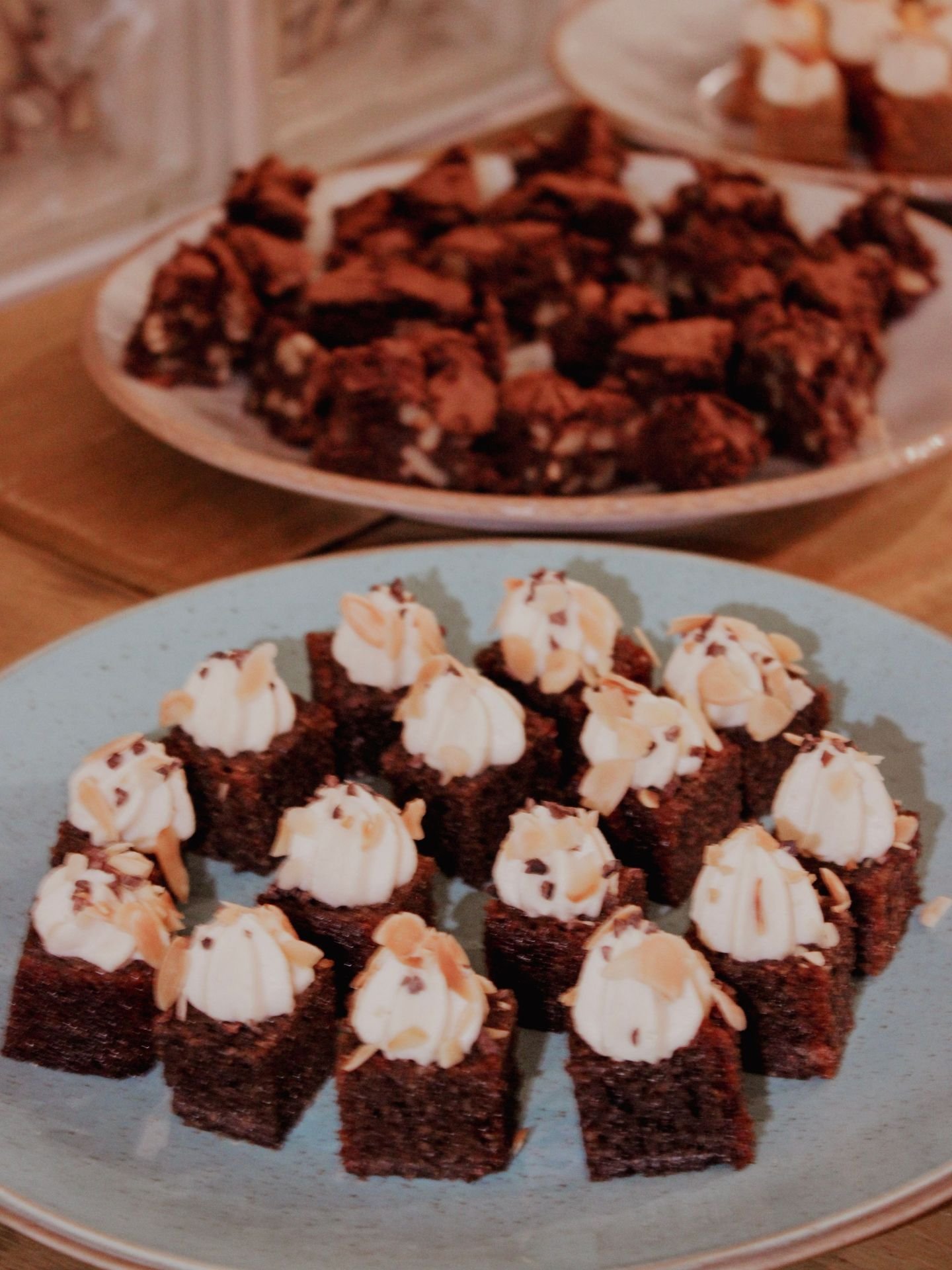 Chocolate gluten-free brownies topped with whipped cream and sliced almonds on a blue plate.