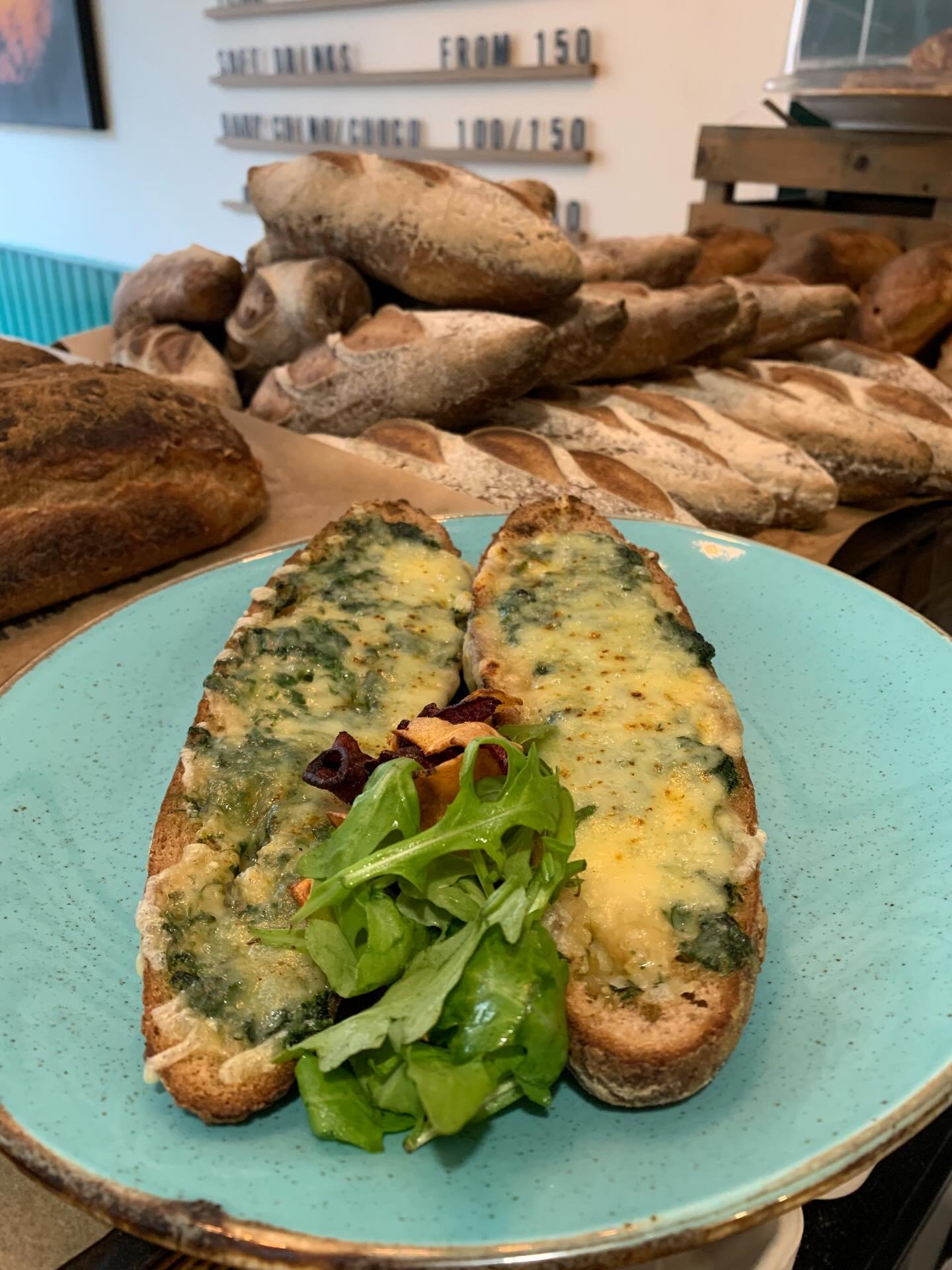 A plate with two slices of toasted gluten-free bread topped with melted cheese and spinach, garnished with a small bunch of arugula.