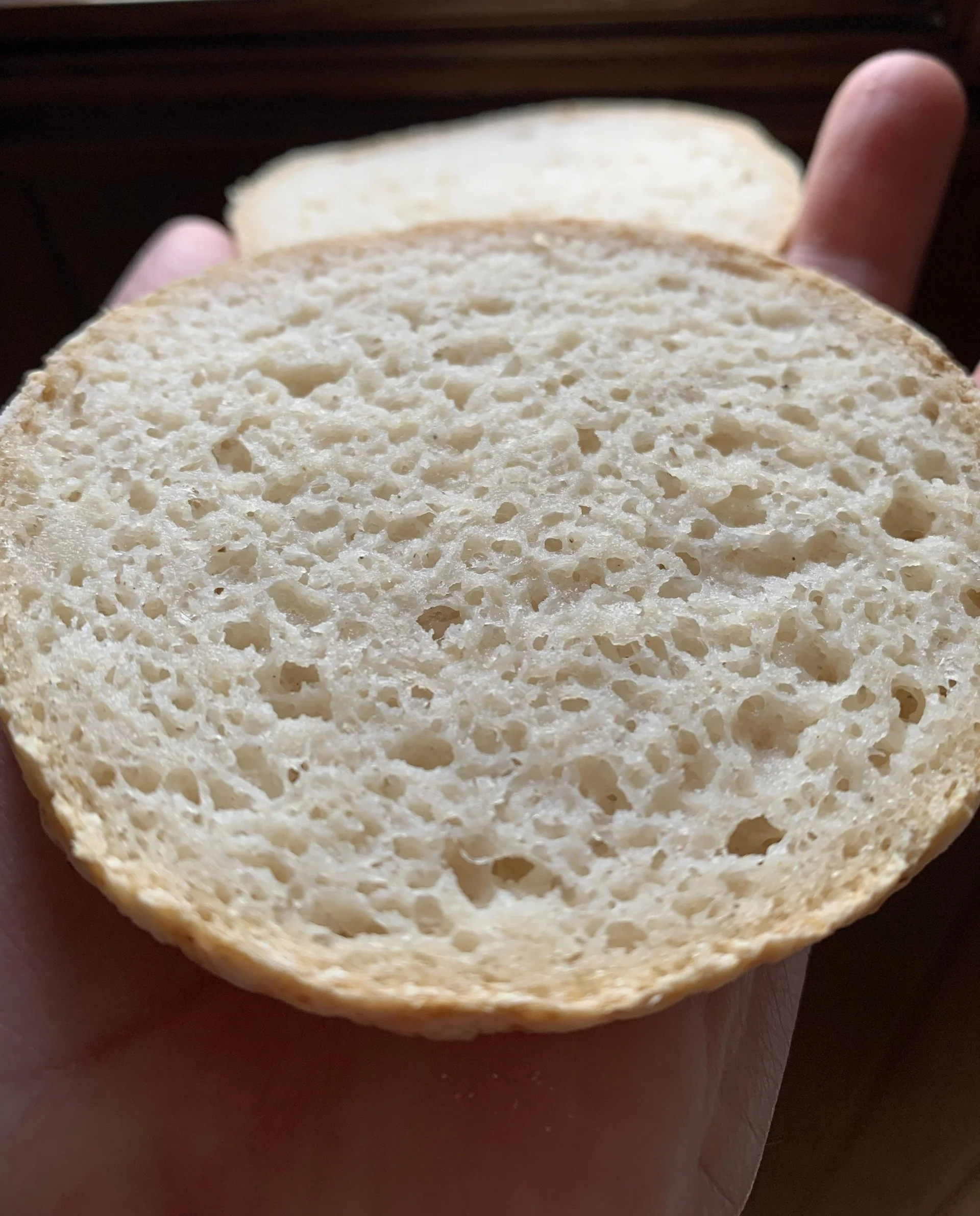 Close-up of a slice of white gluten-free  bread being held by a person, with another slice behind it. The bread has a soft, porous texture. The background is out of focus.