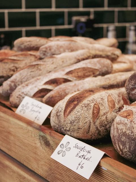 Assorted gluten-free rustic loaves of bread displayed on a wooden counter with handwritten price tags.