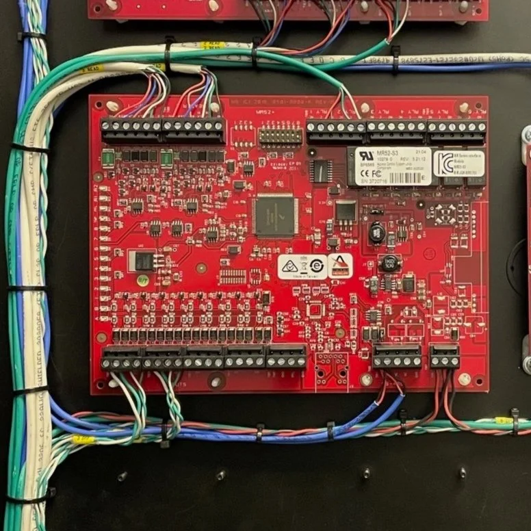 Red circuit board with multiple wiring connections, electronic components, and connectors mounted inside a black enclosure.