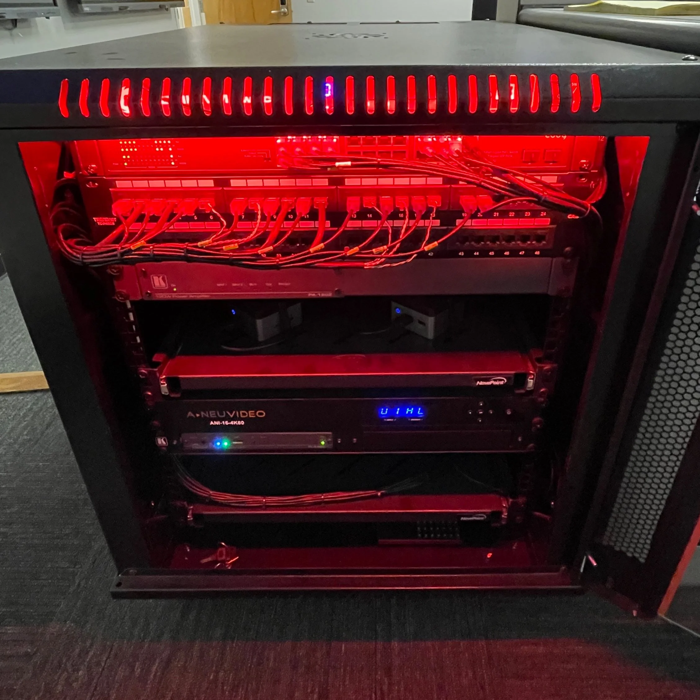 Open server rack with red lighting, showing various network and server hardware including a switch, a video recorder, and other electronic components.