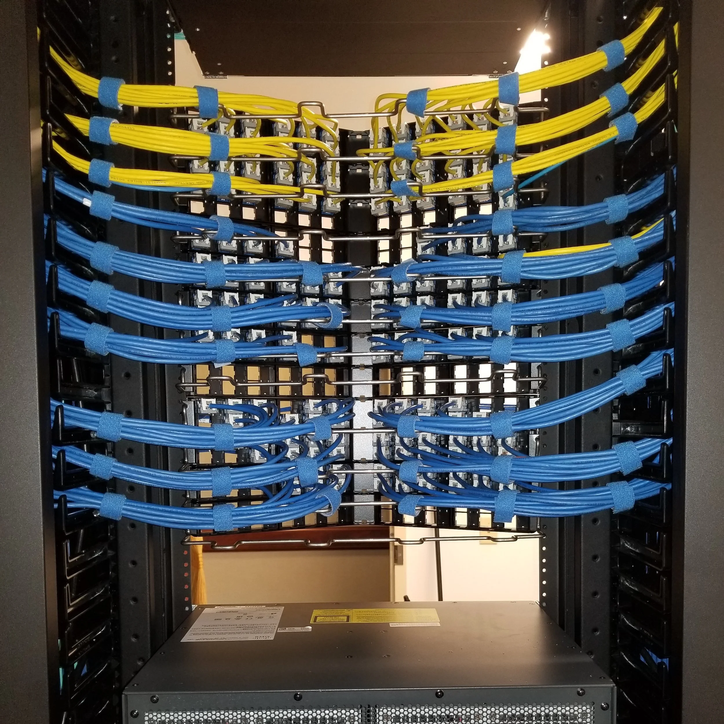A server rack with multiple yellow and blue ethernet cables organized and connected to network hardware.