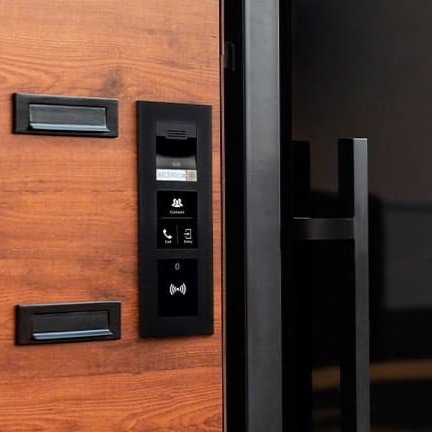 Entry access panel with security system and keypad next to a wooden door with a black handle.