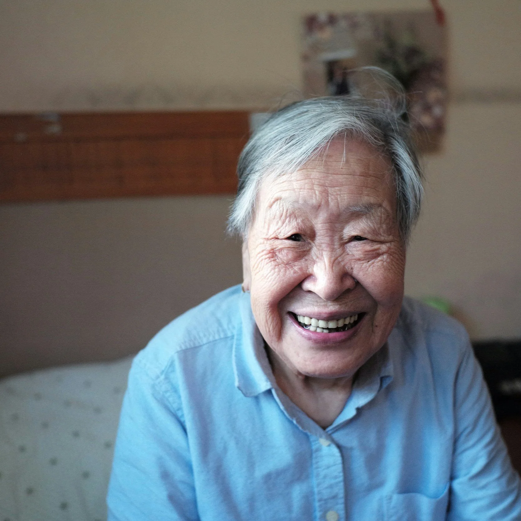 An elderly Asian woman with gray hair smiling warmly indoors.