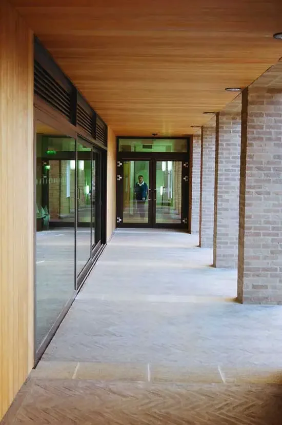 Indoor corridor with glass doors on the left and brick columns on the right.