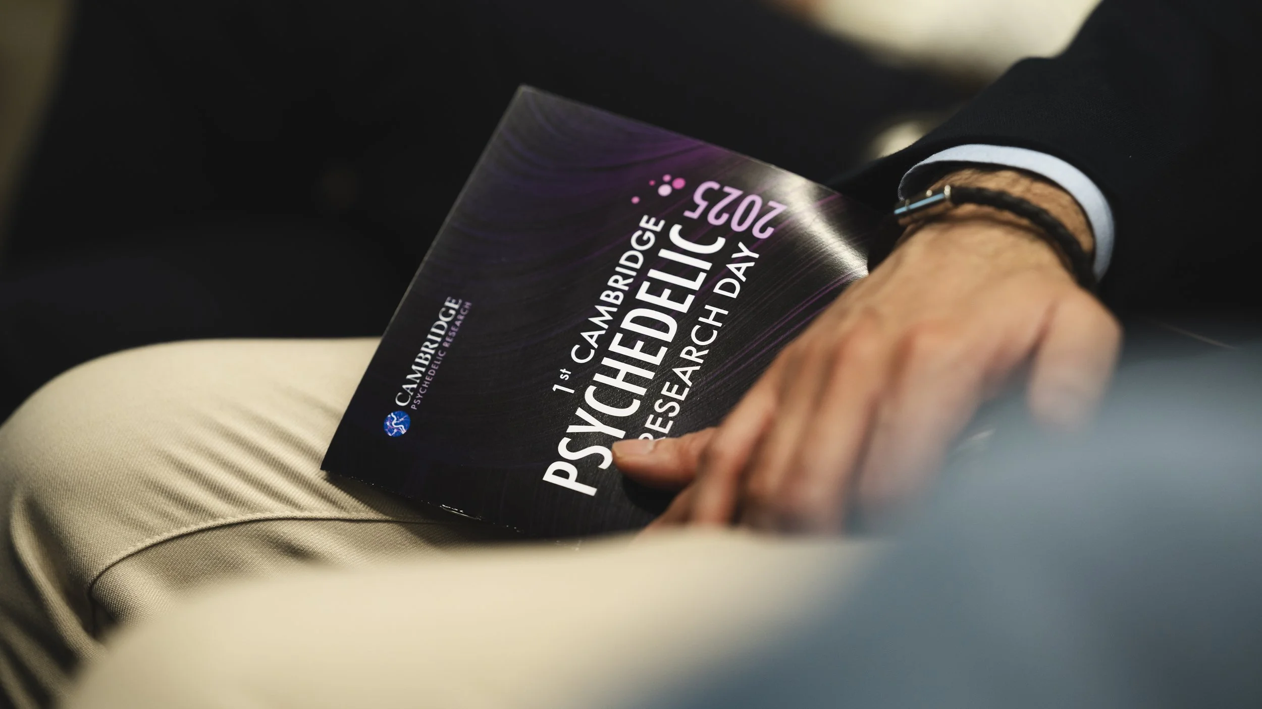 A person holding a flyer or brochure for the 1st Cambridge Psychic Fair 2025, taking place in March.