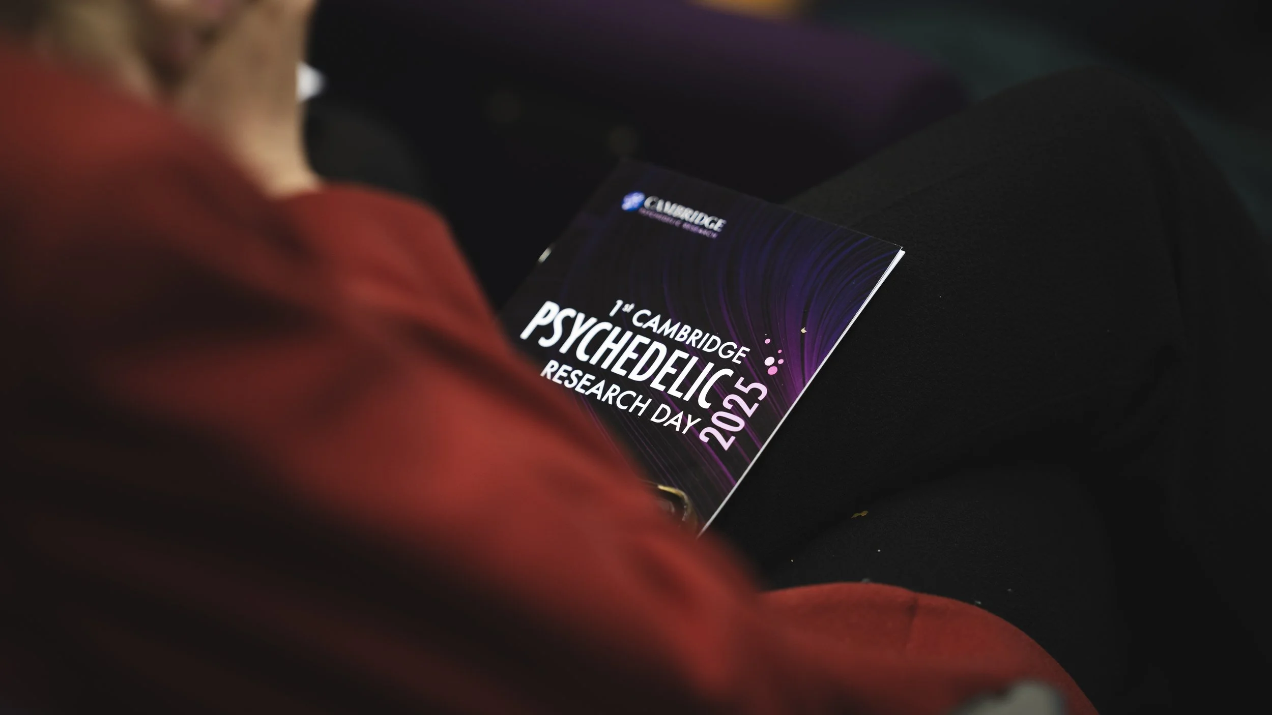 A person holding a conference program for Cambridge Psychedelic Research Day 2022, with the focus on the program and the person partially visible.