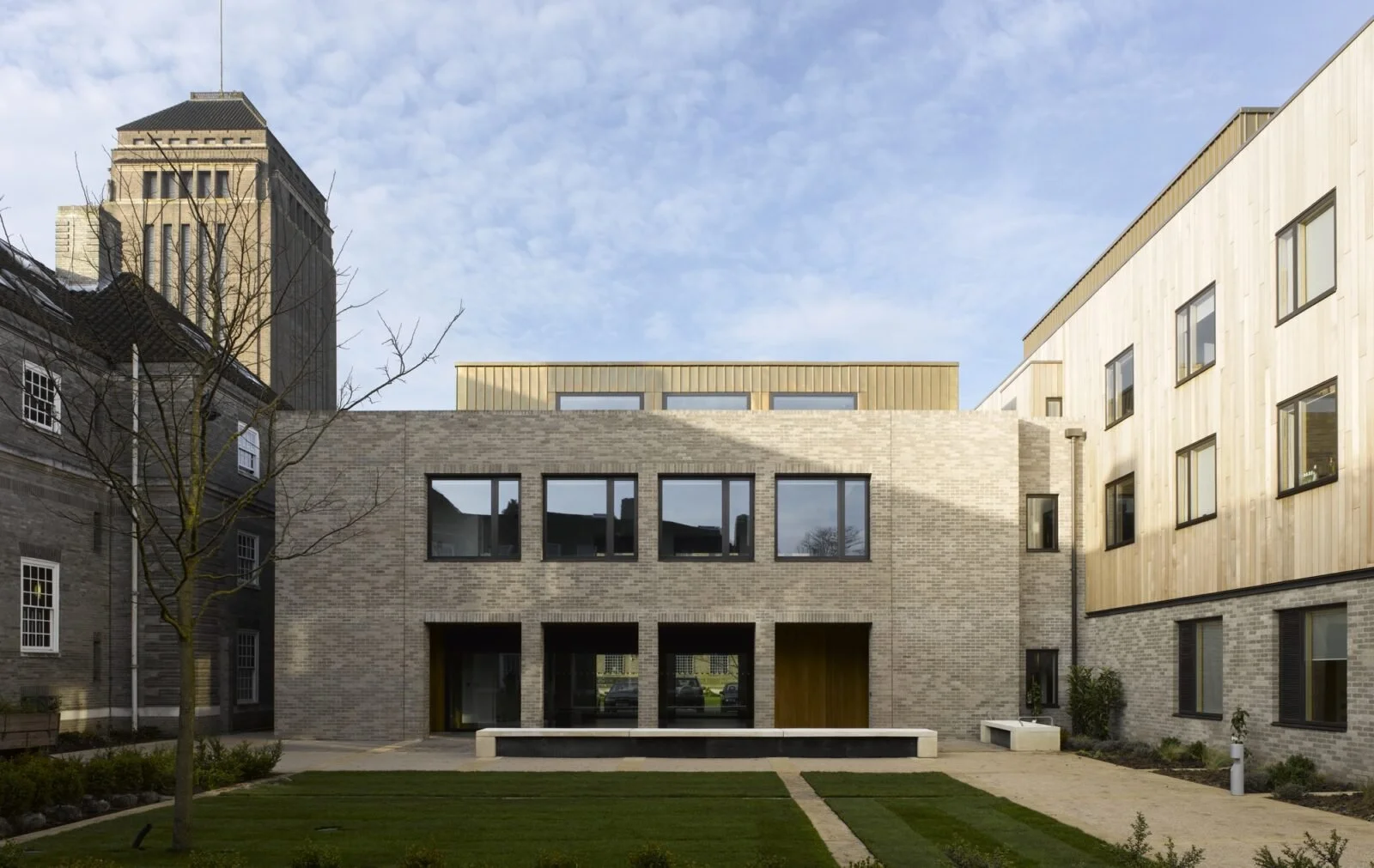 Modern multi-story building with brick and wood facades, large windows, and a landscaped courtyard with pathways and grass.