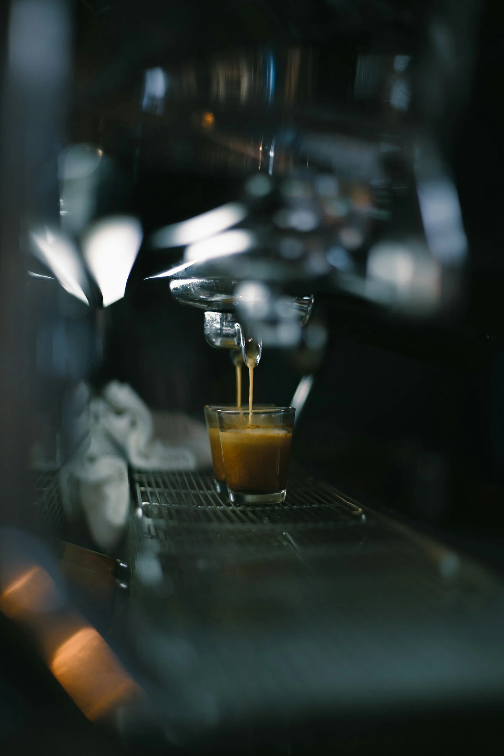 Koffie die uit een espressomachine wordt gezet in een glas, met stoom en koffieapparatuur op de achtergrond.