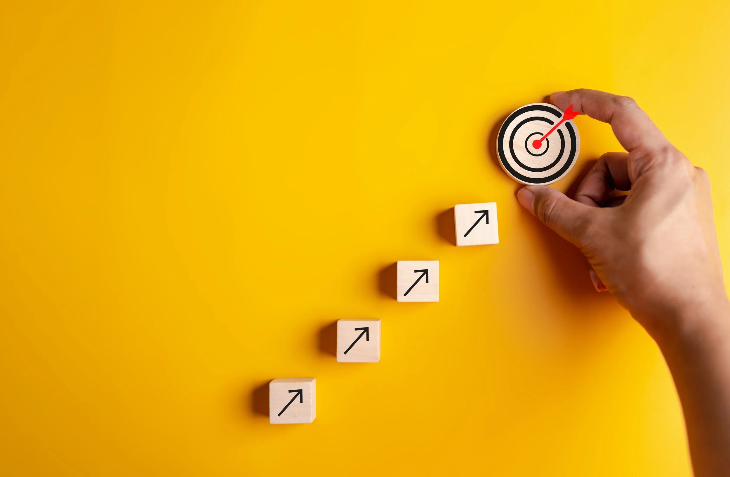 Hand placing target on yellow background with ascending blocks showing arrows