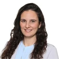 A woman with long dark hair wearing a light blue shirt, smiling at the camera.