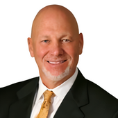 Headshot of a bald man in a black suit, white shirt, and gold tie, smiling against a white background.