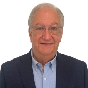 Portrait of a man with gray hair wearing glasses, a navy blazer, and a light blue shirt, smiling against a plain white background.