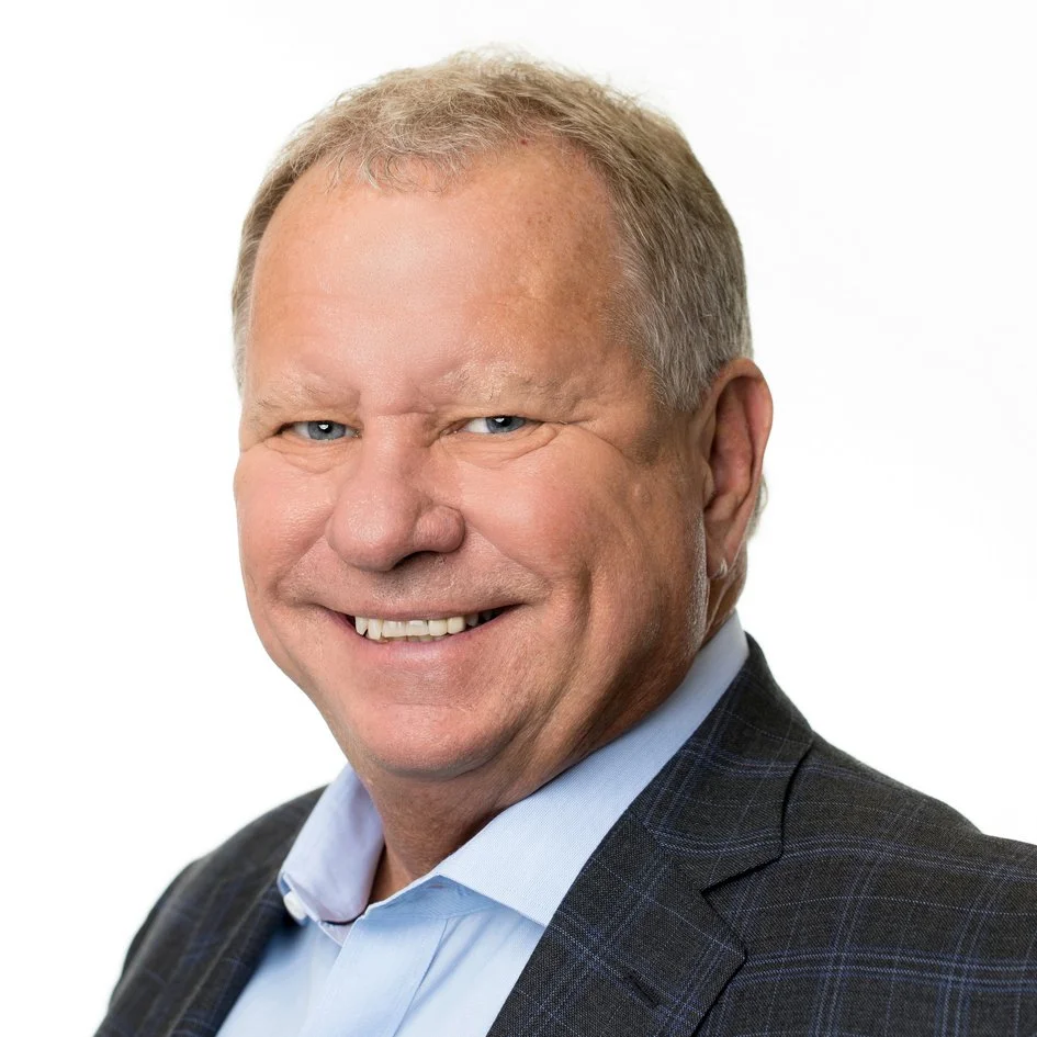 Portrait of a smiling man in a suit with a light blue shirt, against a plain white background.