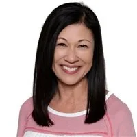 A woman with straight black hair smiling and wearing a pink top.
