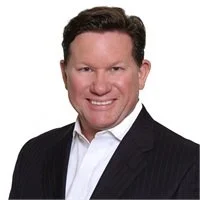 Professional headshot of a smiling man wearing a dark suit and white shirt, with dark hair and light skin