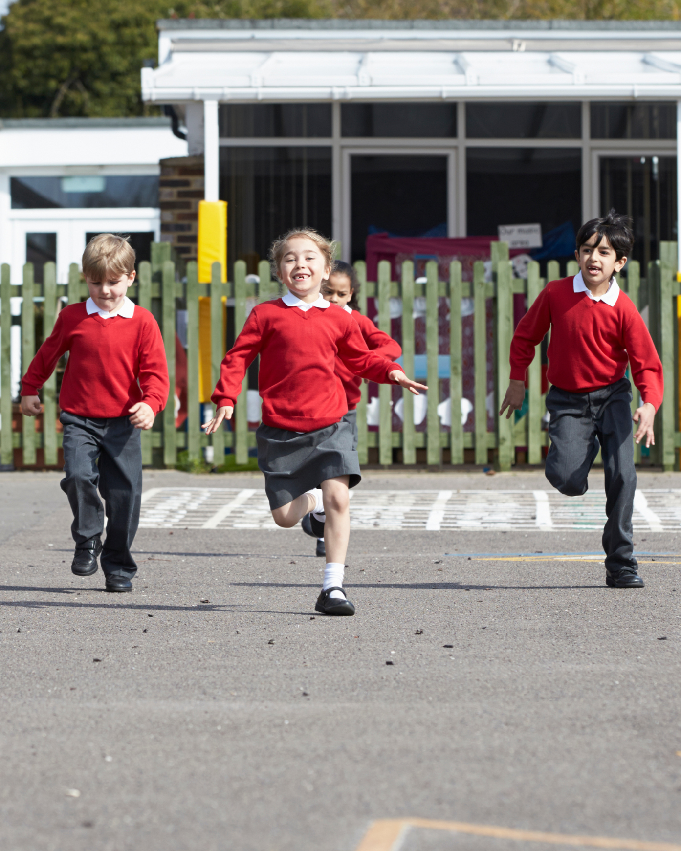 Four children in red school uniforms are running and playing outside on a school playground. 14 Sports Coaching