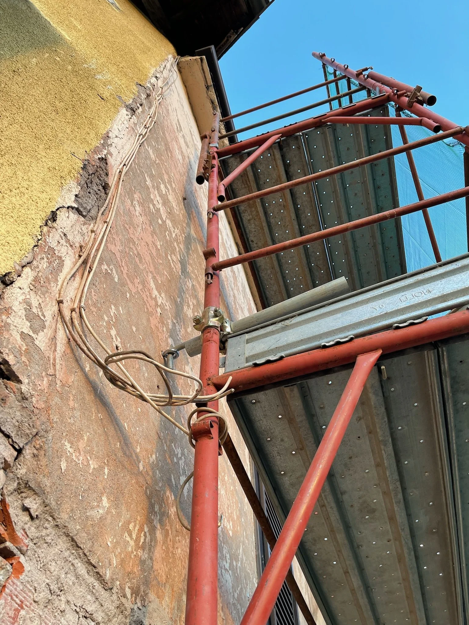 Struttura in metallo rossa con piattaforma di lavoro, scaffalature e cavi elettrici su parete di edificio in fase di ristrutturazione.