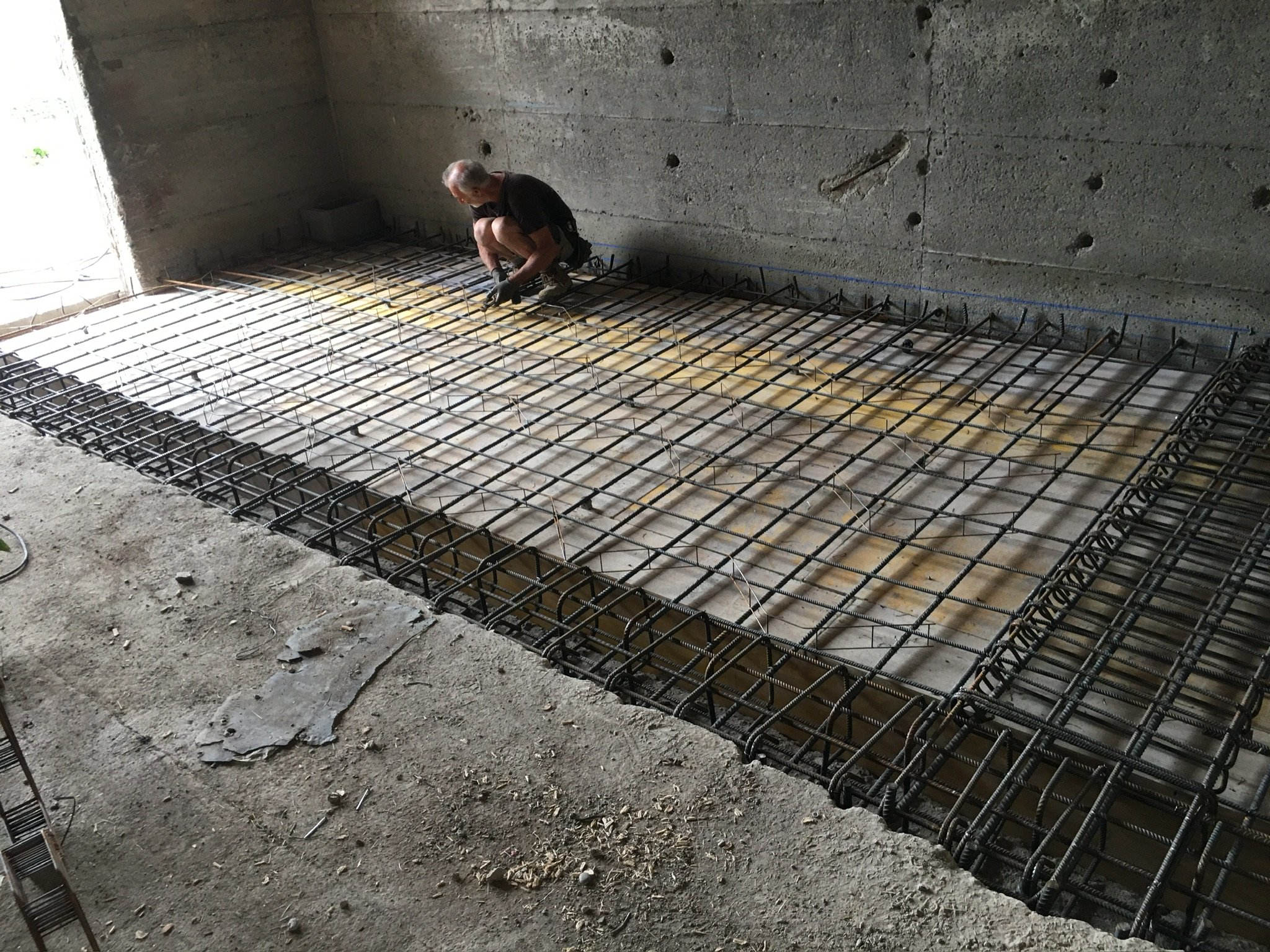 Un uomo che lavora con armature di ferro all'interno di una stanza in costruzione, probabilmente per il cemento armato del pavimento.