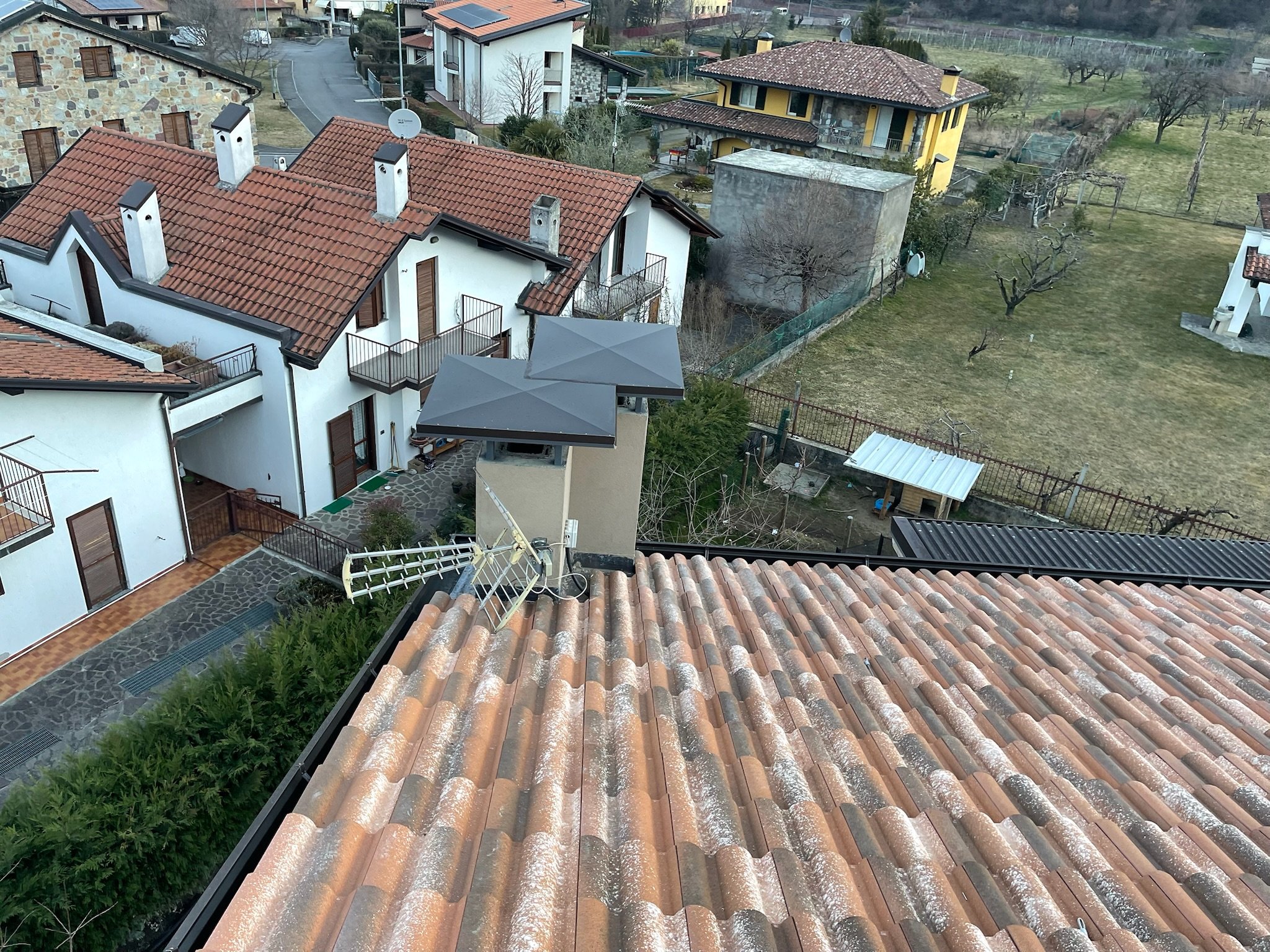 Vista dall'alto di case residenziali con tetti in terracotta, piante e un giardino.