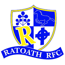 Ratoath R.F.C. club crest with shield divided into four sections, featuring a blue shamrock, a lion, the letter R, and a Greek letter phi, with a banner reading 'RATOATH RFC' at the bottom.