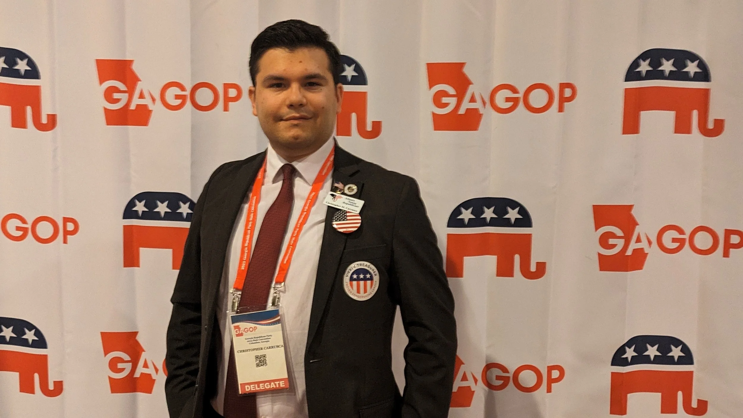Christopher Carruca in formal attire standing in front of a GOP-themed backdrop. 