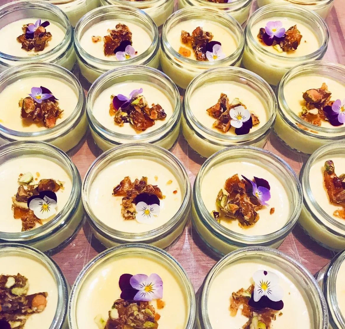 Glass jars filled with creamy dessert, topped with nuts and edible flowers.