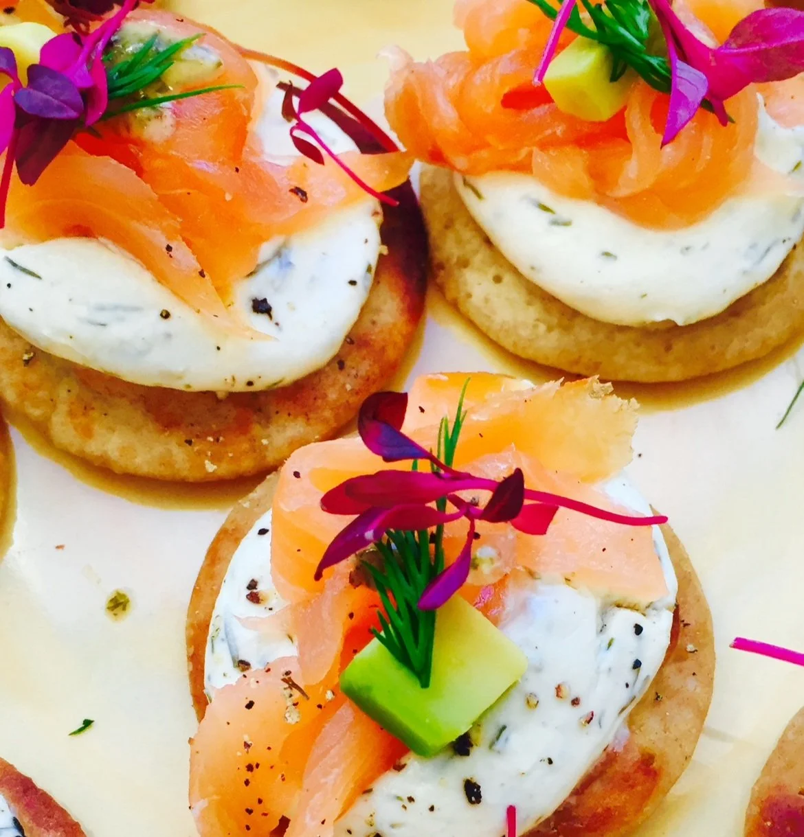 Gourmet appetizers with crackers, cream cheese, smoked salmon, dill, avocado, and edible flowers.