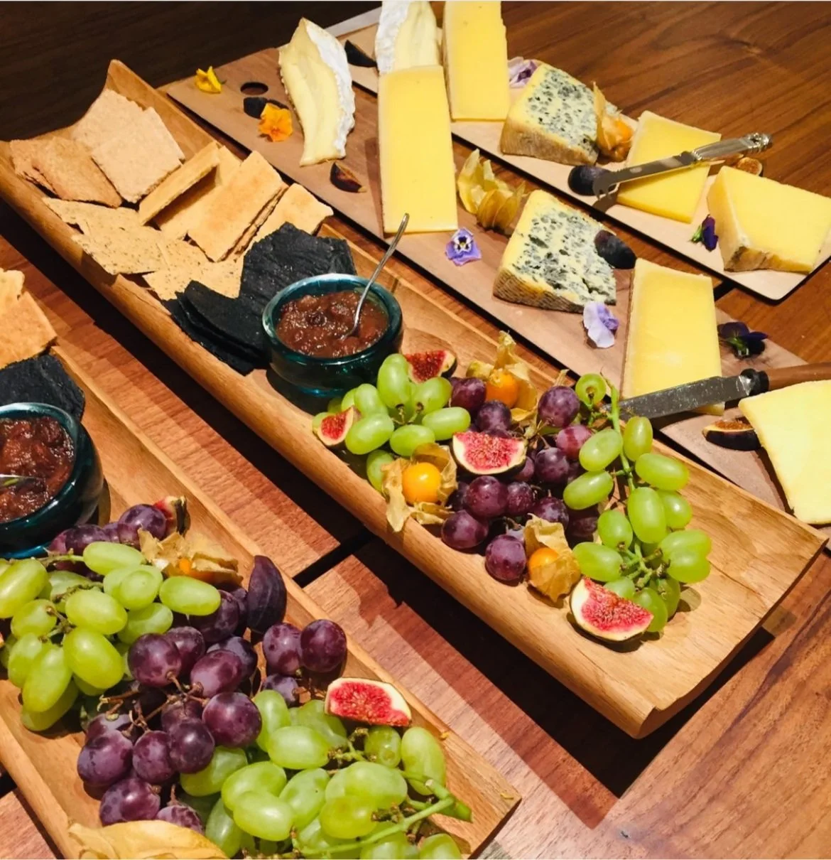 Cheese and fruit platter with assorted cheeses, grapes, figs, crackers, and chutney on wooden boards.