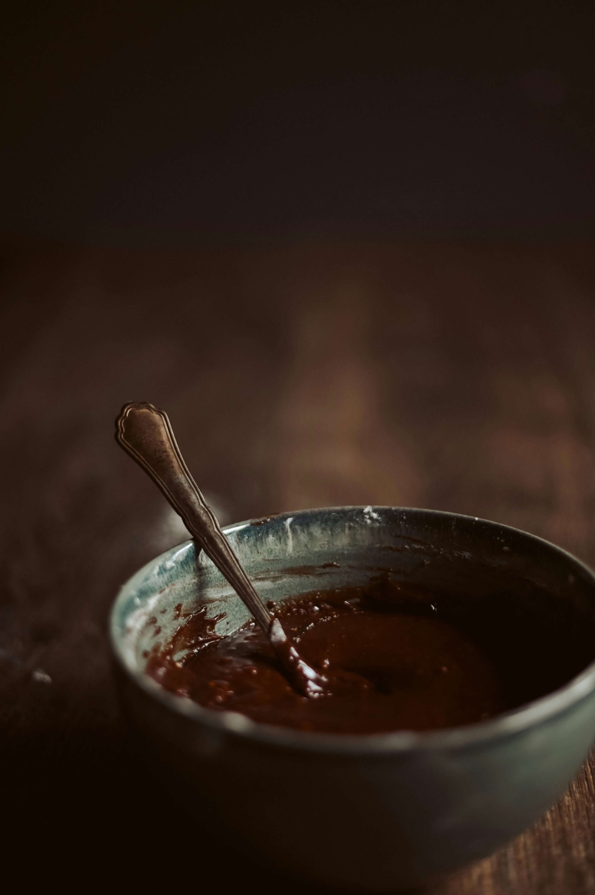 Bowl of melted chocolate with spoon on wooden surface
