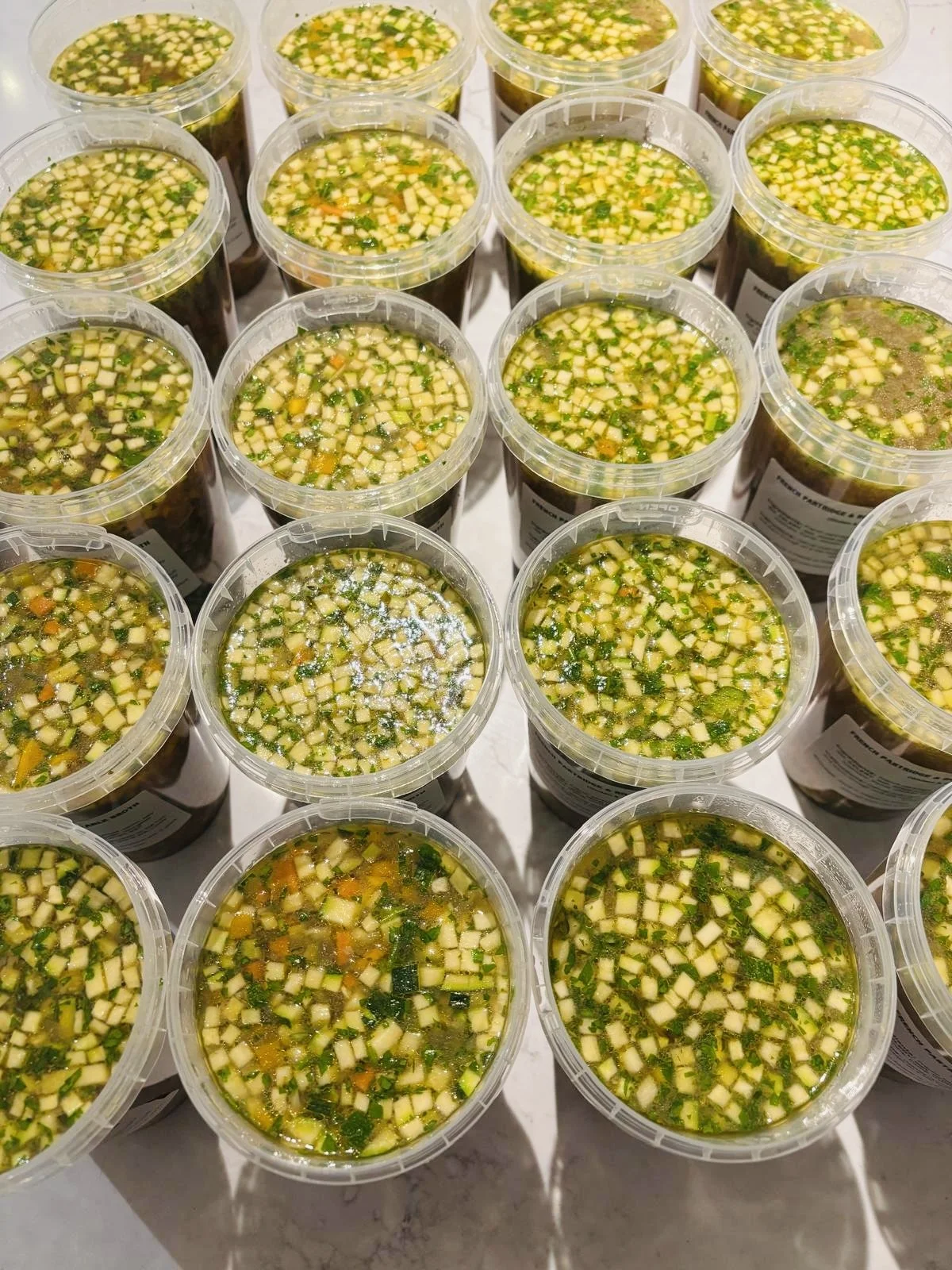 Several plastic containers filled with chopped vegetables and herbs in liquid, arranged on a table.