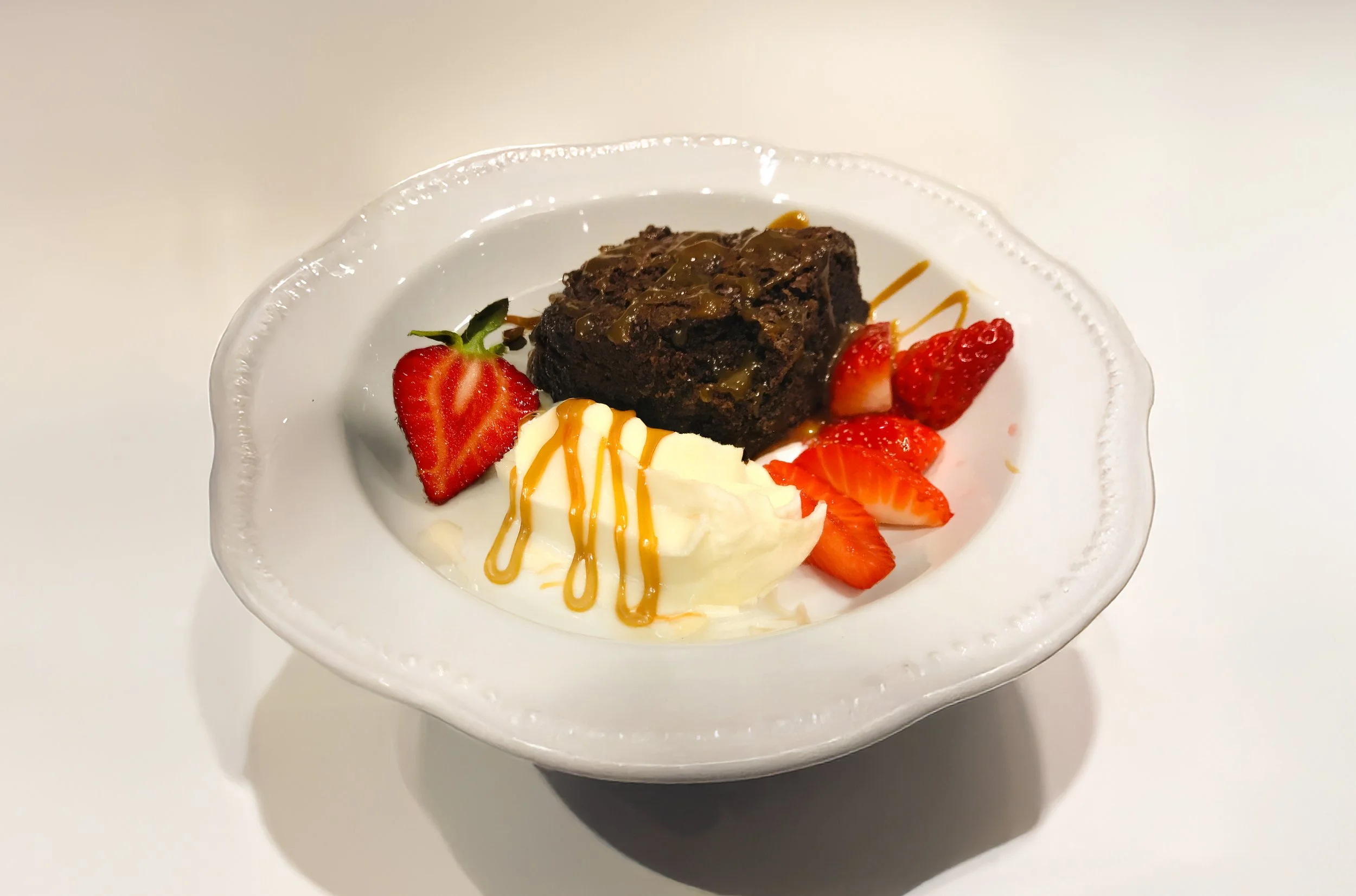 Dessert plate with chocolate brownie, strawberries, whipped cream, and caramel drizzle.