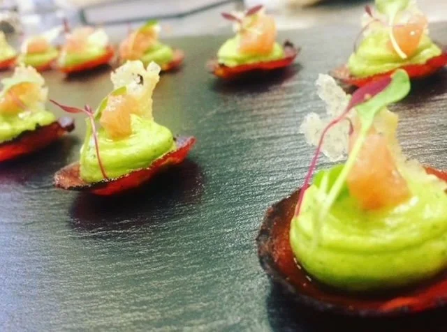Gourmet appetizer with green mousse, salmon, and microgreens on red crisps on a slate plate.
