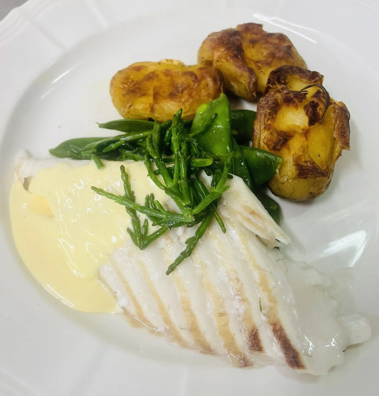 Plate with white fish fillet, sauce, green vegetables, and roasted potatoes