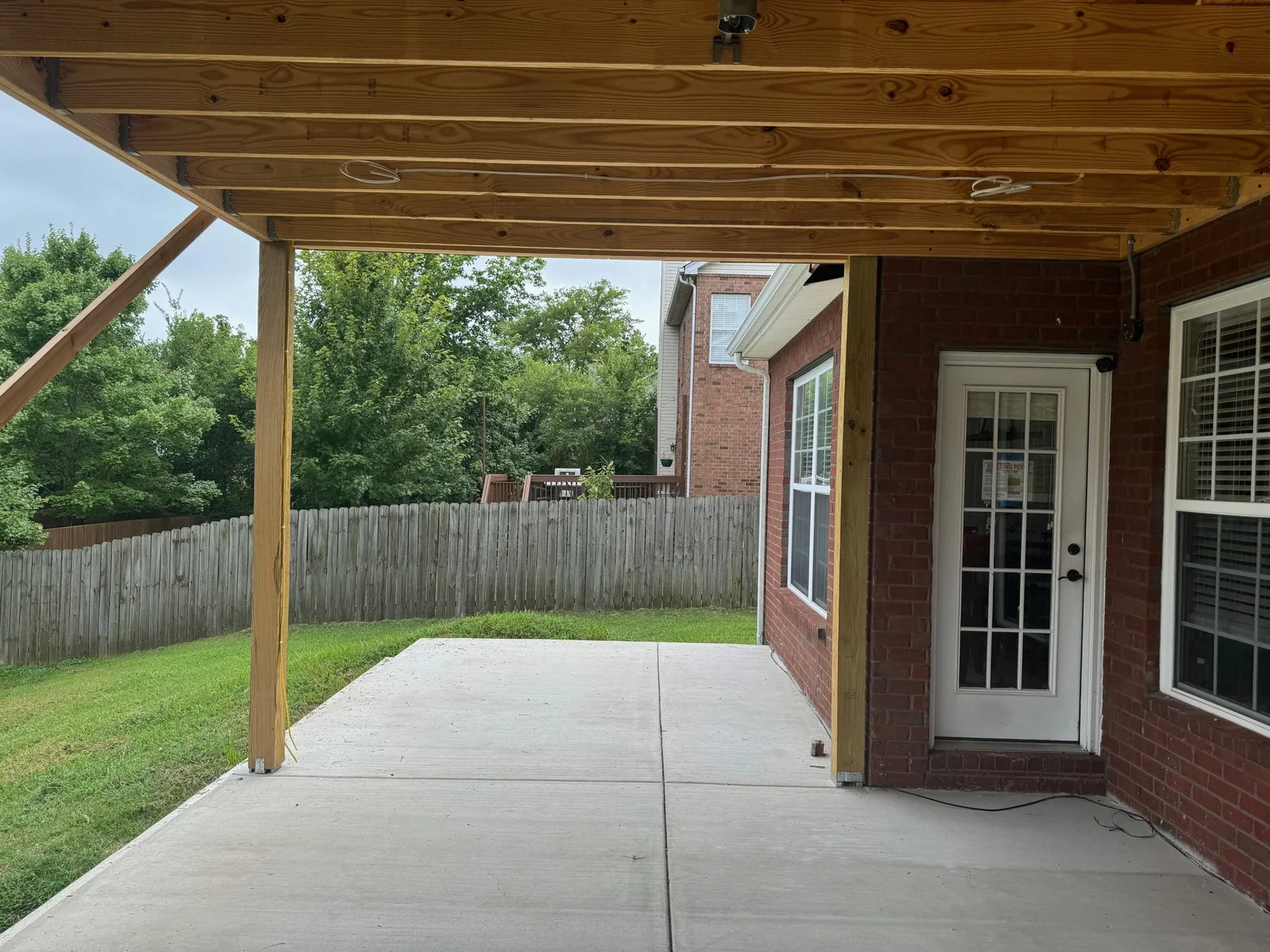 Covered patio with stained wood posts and a poured concrete slab behind a brick home