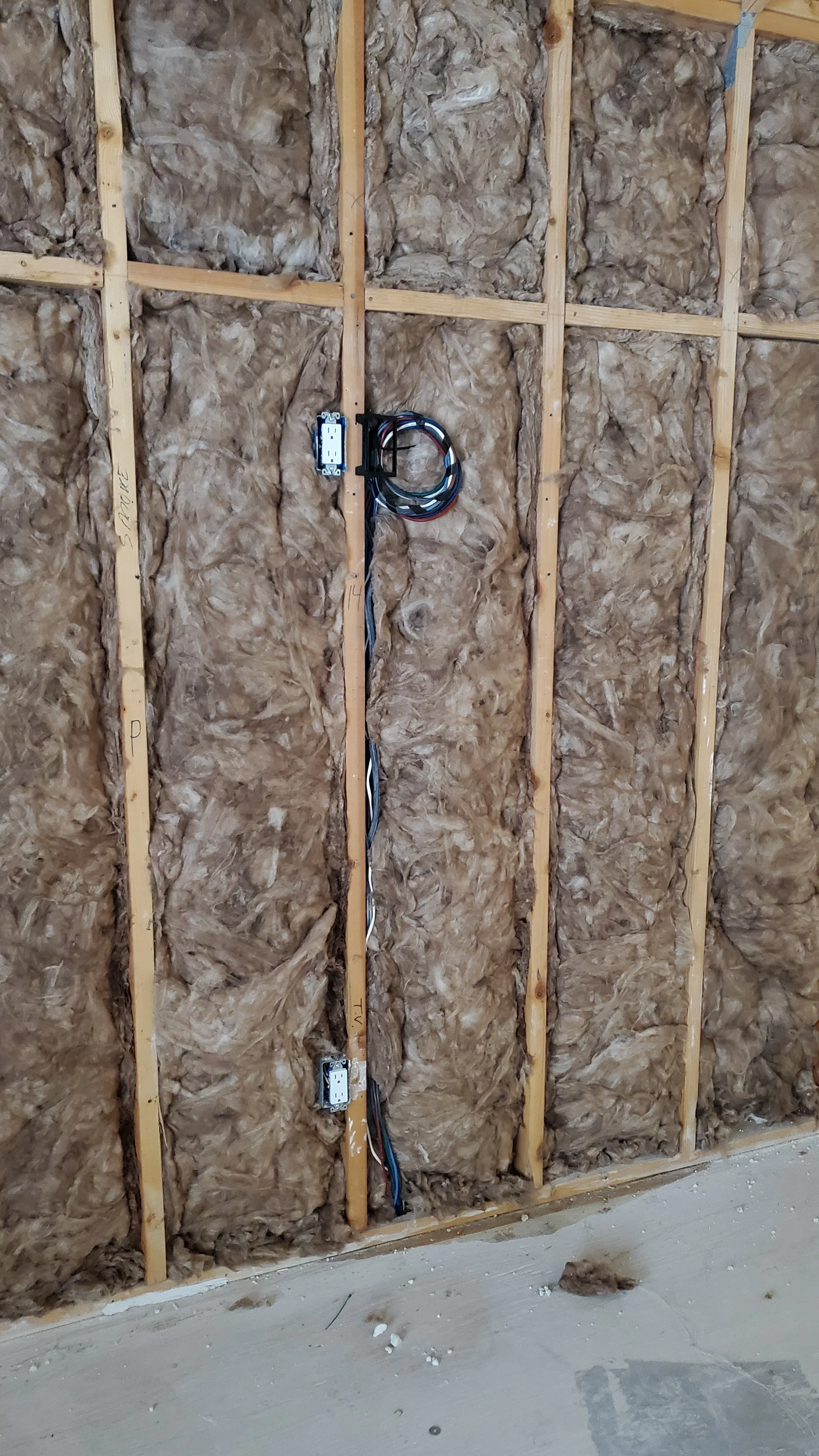 Wall cavity between wood studs filled with pink insulation and a cable running along the top, before drywall in a Memorial, Houston remodel