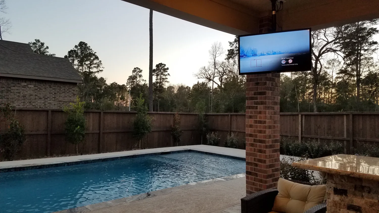 Covered patio with an outdoor TV and pool at sunset