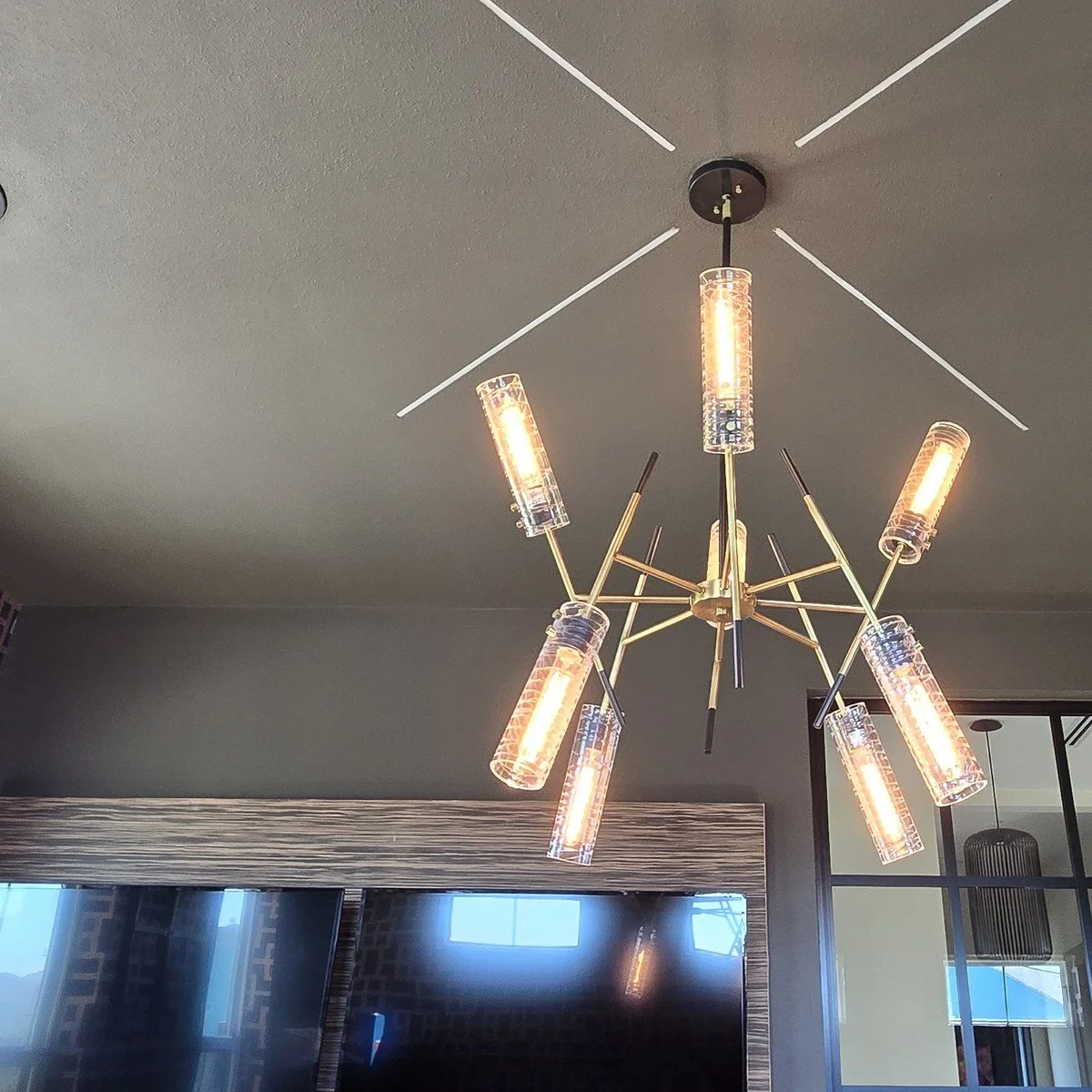 Modern brass chandelier with glass cylinder shades in a finished game room